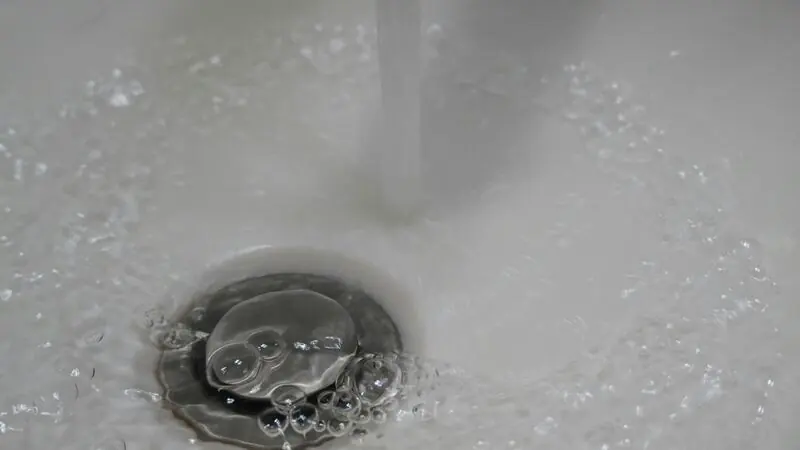Wasserstrahl läuft in den offenen Ablauf eines Waschbeckens.