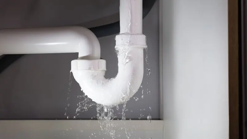 Wasser schießt aus dem gelösten Siphon unter einem Waschbecken auf den Boden.